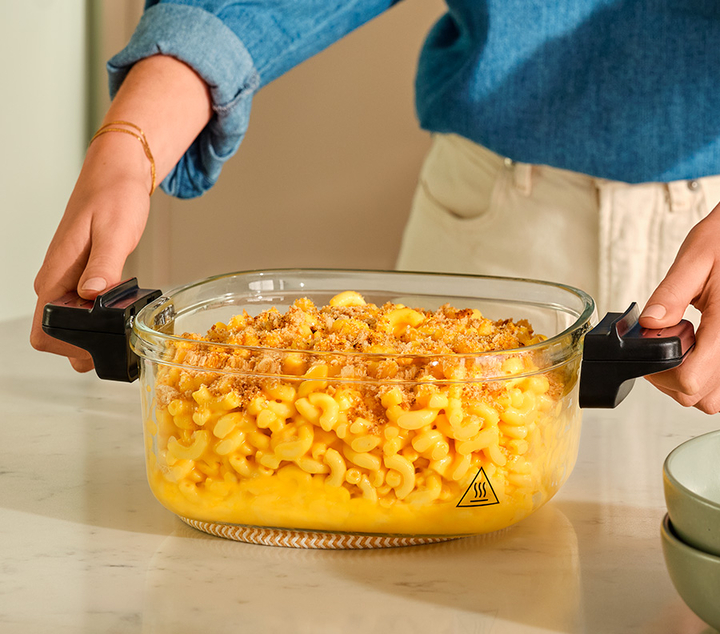 Hands holding 4 quart glass air fryer basket with macaroni and cheese
