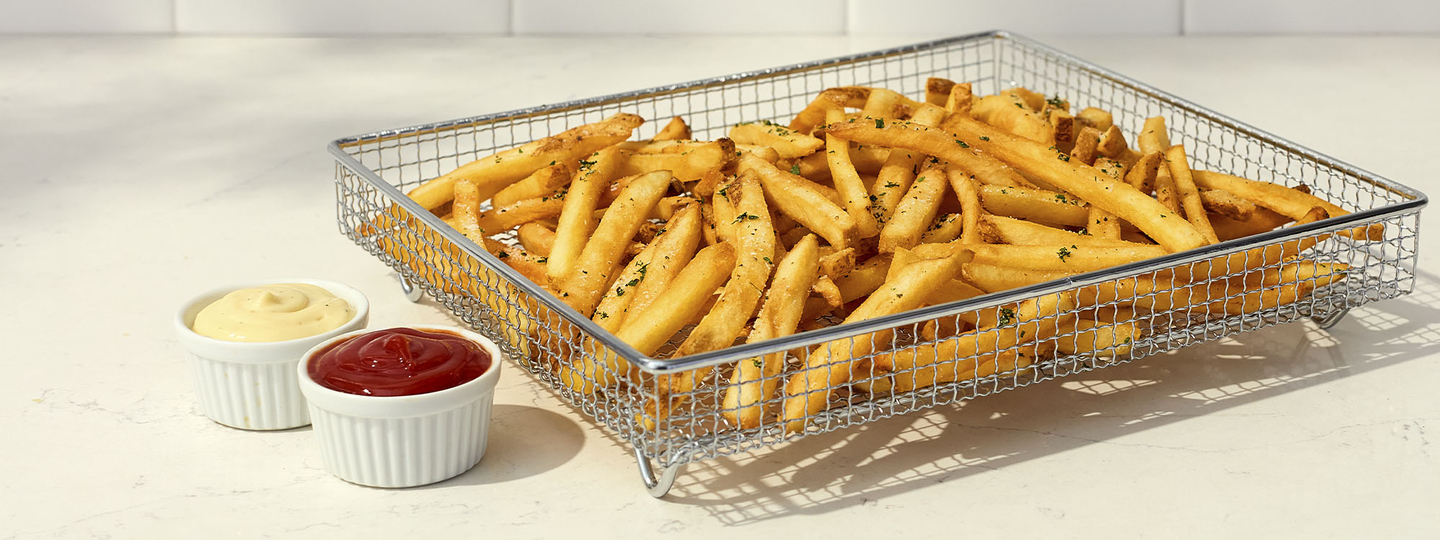 cooked french fries in a wire basked with ketchup in a white bowl