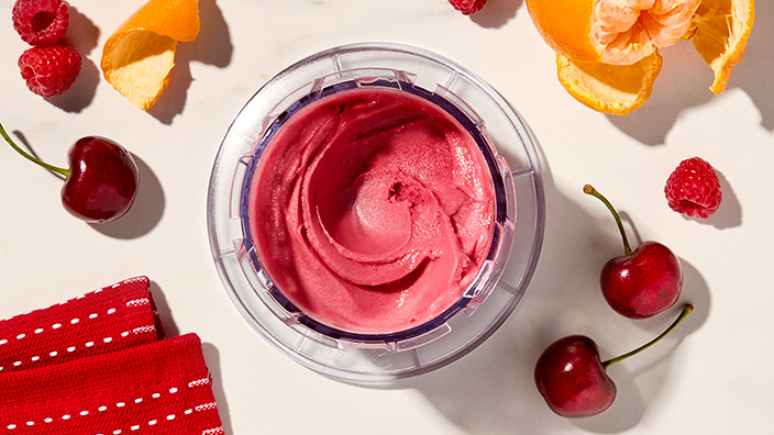 Red sorbet  in container with cherries and oranges nearby.