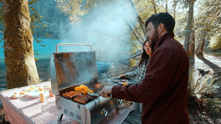 Man and woman using black cuisinart portable grill on beach