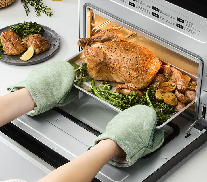 hands in oven gloves pulling a whole roast chicken from the Cuisinart digital air fryer toaster oven