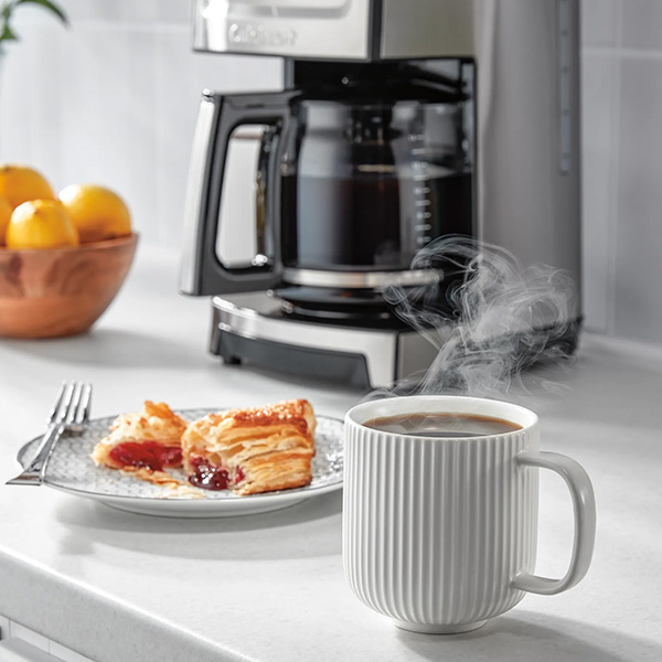 A cup of hot coffee made with Cuisinart coffee maker next to a plate with pastry