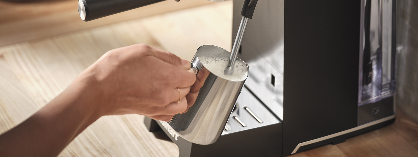 hand holding milk carafe to frothing wand
