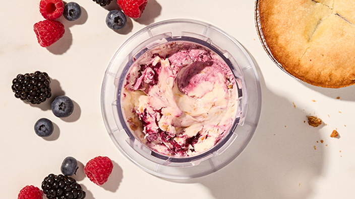 Container of ice cream with fruit and a pie nearby.