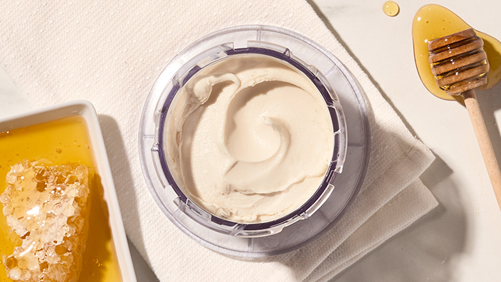 Container of vanilla ice cream with honeycomb and a honey stick nearby.
