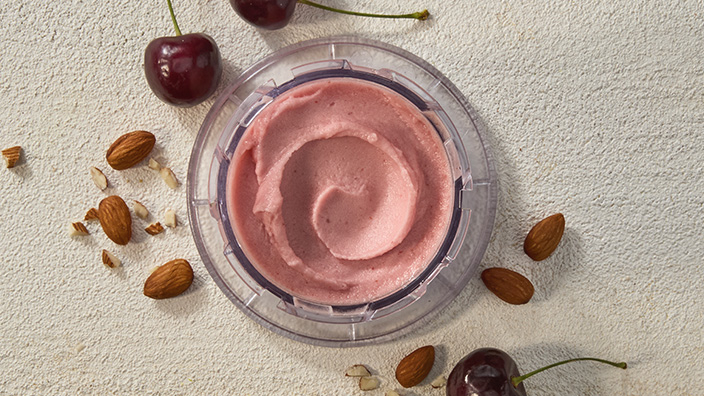Container of frozen yogurt with almonds and cherries nearby.