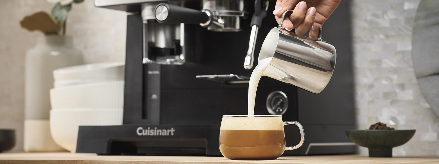 handing holding milk carafe with milk pouring onto coffee cup.