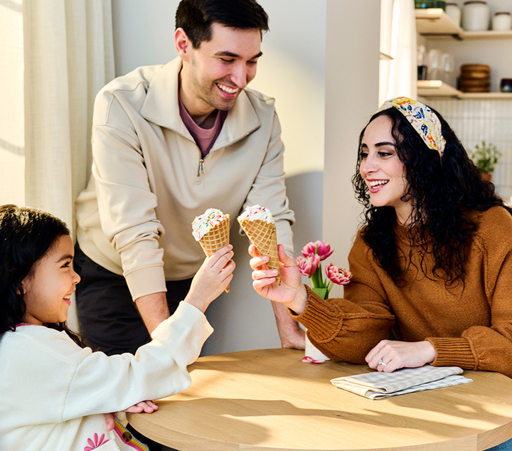 Happy mother and little daughter enjoying ice cream together as dad watches.